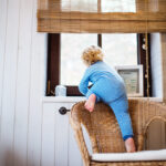 Little toddler boy opening a window. Domestic accident. Dangerous situation at home. Rear view.